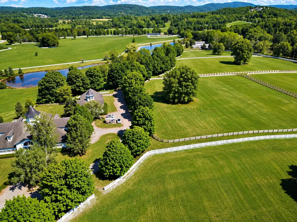Aerial view of a country estate with a pond and white fences